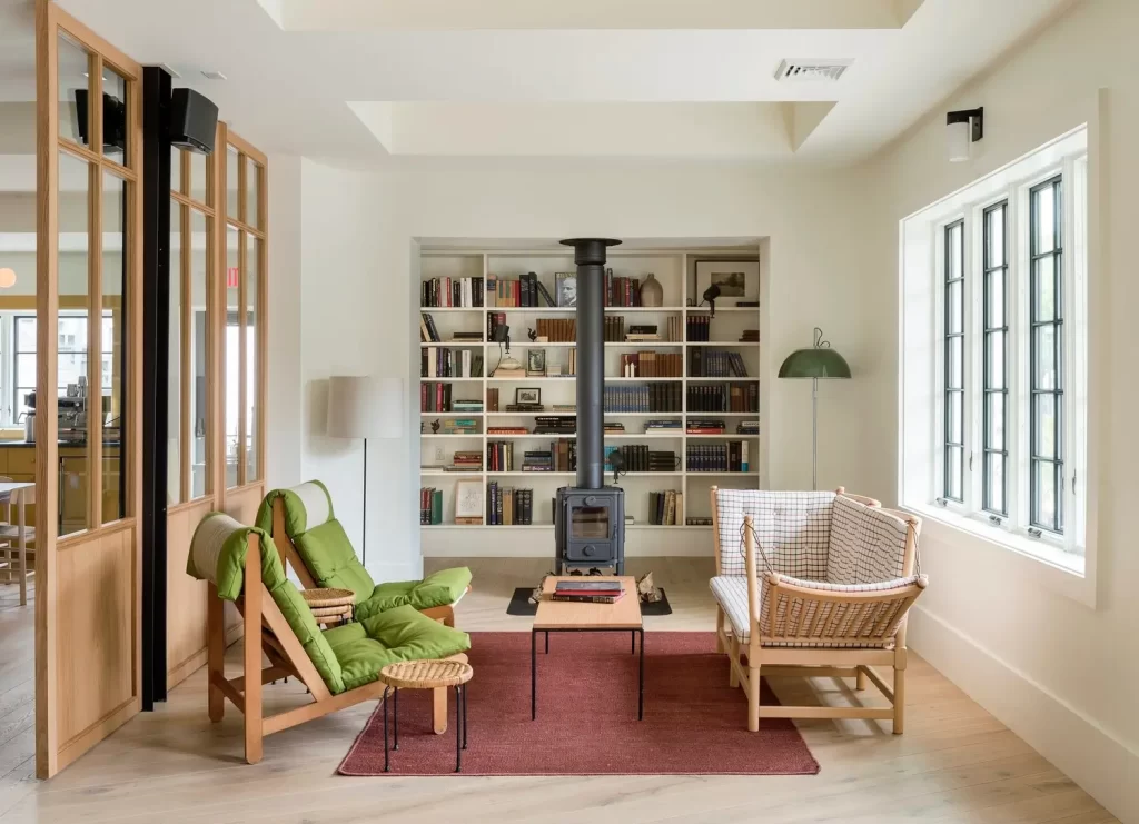 Cozy reading room with green chairs and a wood stove in a modern renovation in Hudson, NY.