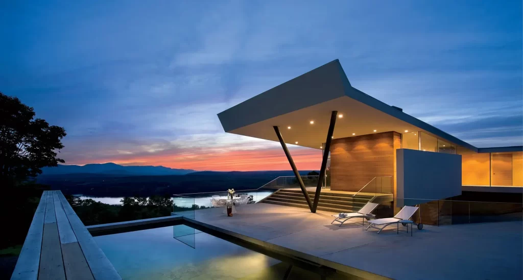 An exquisite custom home in the Hudson Valley, with a dramatic sunset view over the river and mountains, featuring modern architecture and outdoor living spaces.