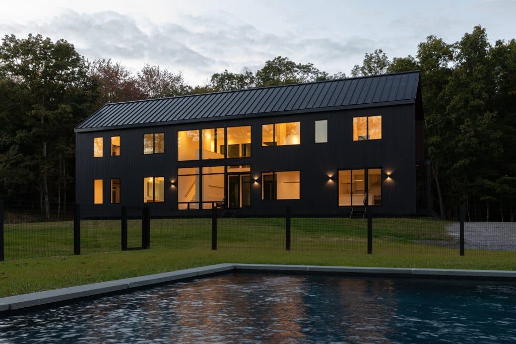 Evening view of a modern custom home build in Hudson, NY with illuminated large windows.