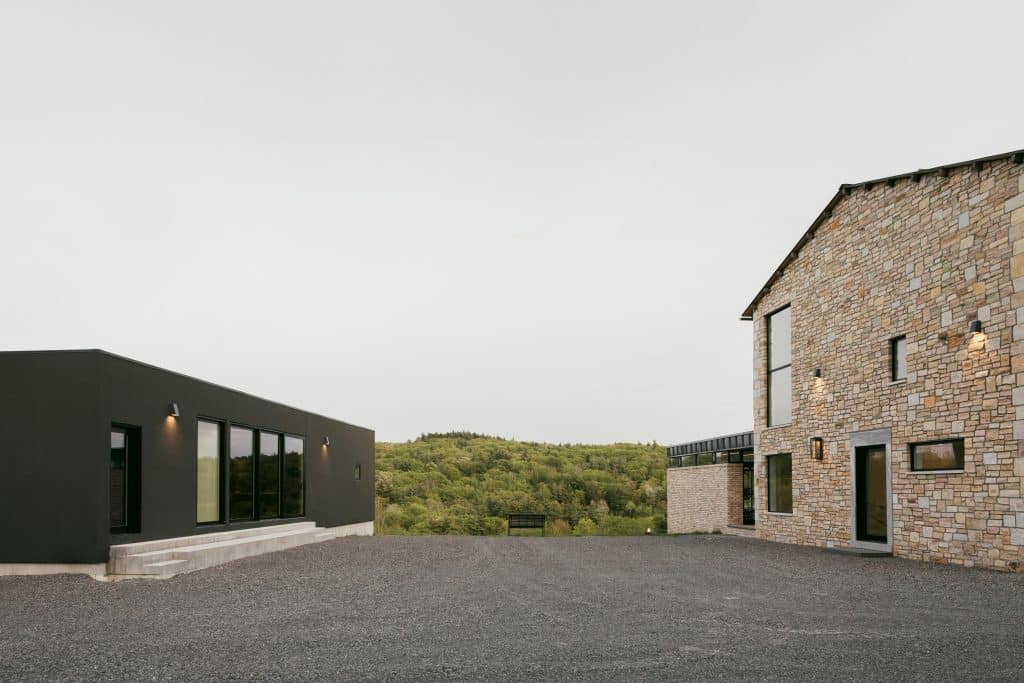 A custom home build in Chatham, NY, featuring a combination of modern and stone elements, large windows, and a spacious outdoor area with views of the surrounding greenery.