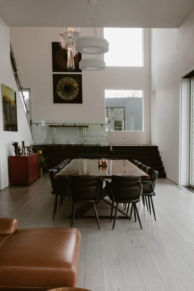 An elegant dining area in a custom luxury home in Chatham, NY, featuring a large wooden dining table, high ceilings, modern art, and sophisticated decor with large windows letting in natural light.