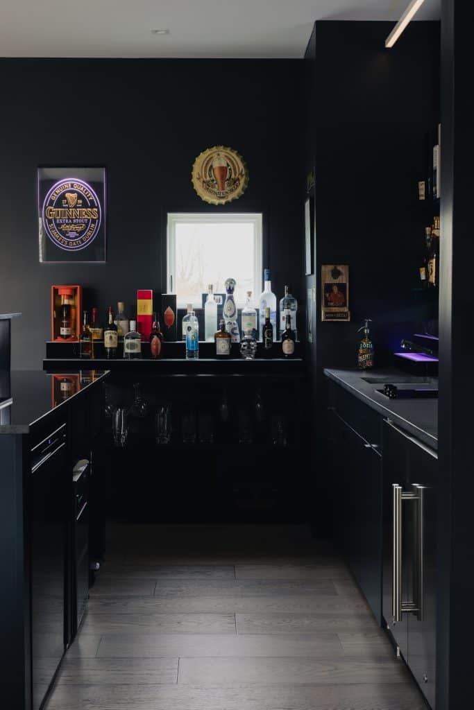 A contemporary home bar in Chatham, NY, featuring modern decor with sleek black cabinetry, a well-stocked selection of spirits, and stylish lighting in a custom home build.